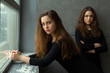 © Alexandr - portrait of two beautiful young girls sisters twins with flowing hair against a gray wall in the interior near the window