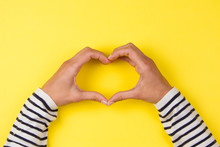Woman hands making a heart shape on yellow background