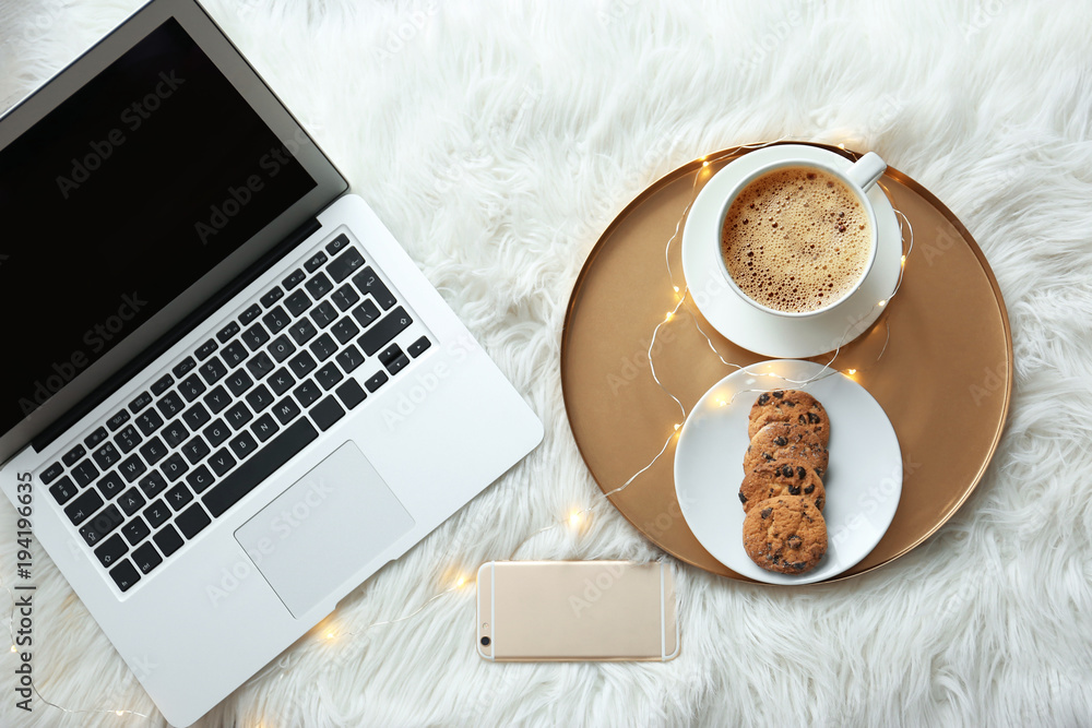 Laptop, mobile phone and tray with breakfast on fluffy carpet, top view