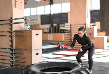 Wall Mural - Young muscular woman hitting heavy tire with hammer in gym