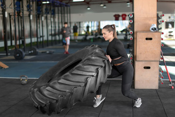 Wall Mural - Young muscular woman flipping heavy tire in gym