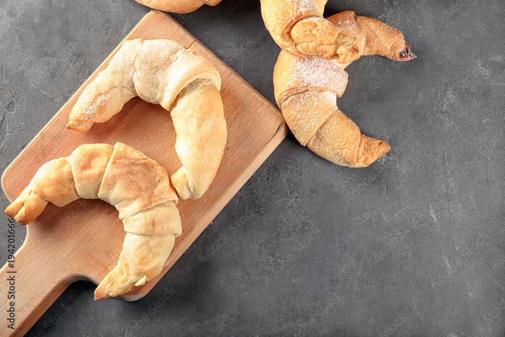 Wooden board with tasty crescent rolls on grey background