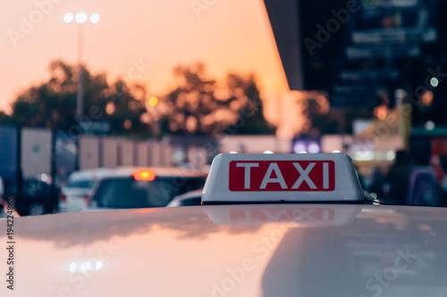 Fotografía Taxi sign on the roof of taxi cab on the busy street over yellow orange warming sunset background