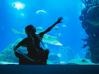 Wall Mural - Girl watching fish through the glass in Oceanarium