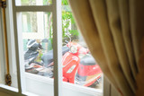Fototapeta  - Red motorbike parked in a yard. View from the window
