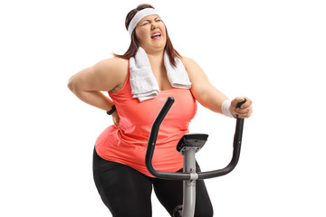 Wall Mural - Overweight woman riding an exercise bike and experiencing back pain