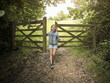 © Maskot - Full length of smiling girl standing by wooden gate on footpath amidst plants