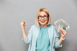 © Drobot Dean - Happy middle-aged blonde woman in blouse and eyeglasses holding money