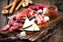 Cured Meat And Cheese Platter Of Traditional Spanish Tapas - Chorizo, Salsichon, Jamon Serrano, Lomo And Slices Of Goat Cheese - Served On Wooden Board With Olives And Bread Sticks