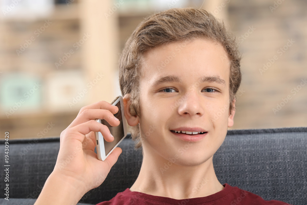 Teenage boy with hearing aid talking on phone indoors