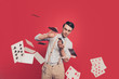 Professional, cunning magician, illusionist, gambler in casual outfit, glasses, throwing, sending cards to the camera, standing over red background