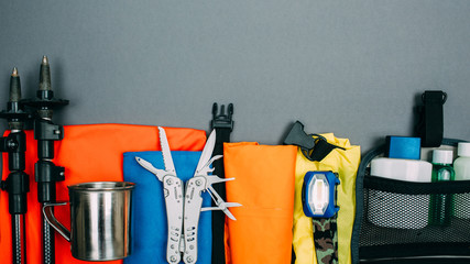 Top view of equipment for hiking and travel on Gray background with copy space . Items include trekking pole, multi tool, flashlight, hygiene products, tracking clothes