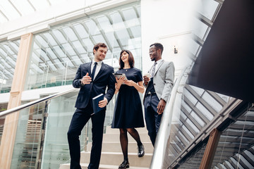 Three happy multiracial business people walking down on stairs together with digital tablet