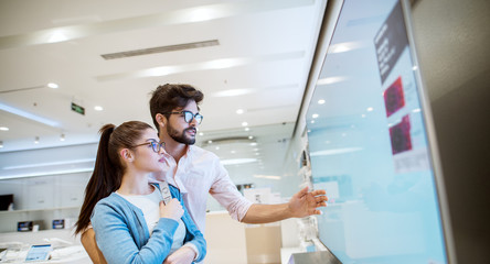 Wall Mural - Joyful young attractive multiracial couple checking out plasma TVs in the electronic store.