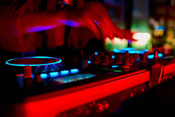 Close up view of the blurry hands of a female disc jockey mixing music on his deck with his hands over the vinyl vinyl record on the turntable and the control switches at night.