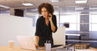 © Mark Adams - Businesswoman using laptop computer in office while listening on smartphone device