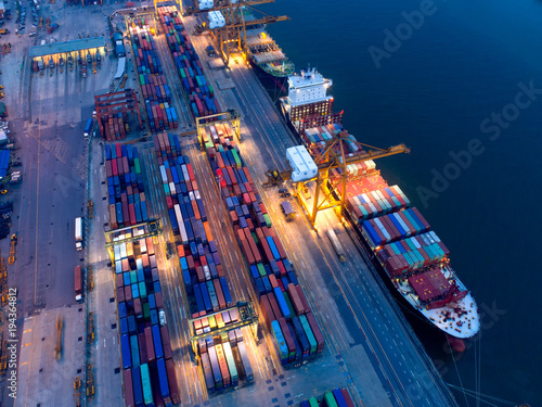 Fotografia, Obraz Container in import/export and business logistics,by crane,Trade port,Shipping cargo to harbor,Aerial view from drone,International transportation,Business logistics concept