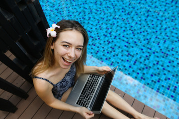 Wall Mural - female woman smilling looking at camera with laptop on background of pool, picture taken from above.