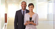 © Mark Adams - African American man and woman posing for a portrait in their office building. Black business couple holding a tablet in a corporate hallway