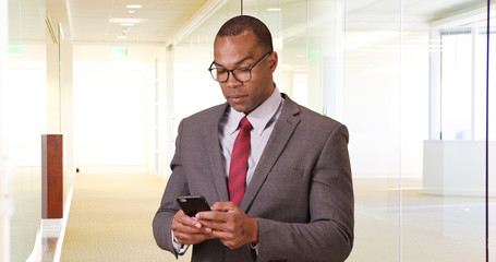 Wall Mural - A black man uses his phone for business. An African American business professional works on his mobile phone and then looks at the camera