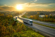 Silver trucks driving on the highway winding through forested landscape in autumn colors at sunset