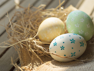 Close up of white color and blue flower pattern, green color and white flower pattern and yellow marble pattern painted Easter eggs on natural bird nest on wooden table with morning sunrise light