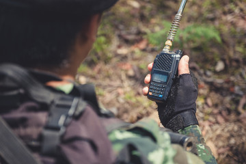 Closeup image of an armed soldier holding and using radio communication in the battle field