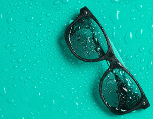 Wall Mural - Fashion sunglasses in drops of water on a bright blue background. Top view.