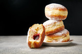Fototapeta  - A stack of three sufganiyot donuts with jelly on black background