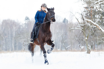 Young rider girl on bay horse galloping in winter. Equestrian winter activity background