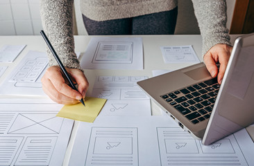 web designer working at laptop and website wireframe sketches on white table
