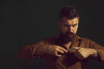 Brutal caucasian hairdresser demonstrating sharp blade of barbershop accessory. Professional barber with thick beard and mustache, holding straight razor. Copy space to advertise barbershop.