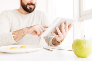 Sticker - Portrait of blurry adult man in casual shirt having healthy meal with frying eggs in apartment, while using digital tablet