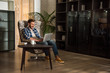 © LIGHTFIELD STUDIOS - Man sitting in armchair and using laptop in living room with design interior
