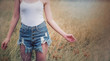 Cropped image of young woman in white vest and short blue jeans standing in the meadow field.