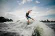 © fesenko - Athletic guy wakesurfing on the board down the river against the sky