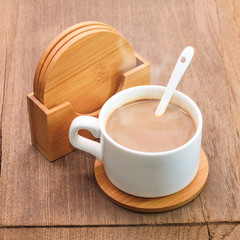 Coffee mug and beverage coaster on wooden background.