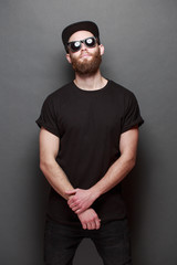 Wall Mural - Hipster handsome male model with beard wearing black blank t-shirt with space for your logo or design over gray background