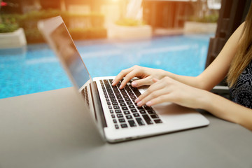 Wall Mural - Fingers typing on the computer keyboard. Close up portrait of woman hands pressing buttons on laptop at sunny day swimming pool. concept of business freelance working, new technologies