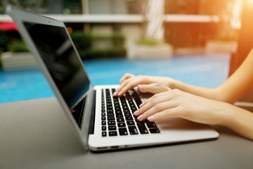 Wall Mural - concept of business freelance working, new technologies. Fingers typing on the computer keyboard. Close up portrait of woman hands pressing buttons on laptop at sunny day swimming pool.