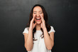 © Drobot Dean - Image of pleased asian woman in casual t-shirt shouting or calling putting hands at mouth, isolated over dark gray background