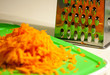 Carrots grated on a metal grater on a cutting board of green color