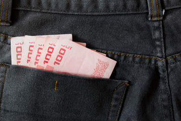 Thailand money including 100 baht in back pocket of a man's black charcoal jeans pocket.