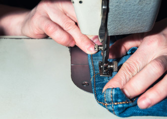 Wall Mural - hands of an elderly seamstress working with jeans on a sewing machine