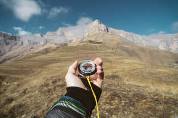 Viewpoint shot. A first-person view of a man's hand holds a compass against the background of an epic landscape with cliffs hills and a blue sky with clouds