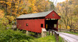 Covered bridge on dirt road with colorful Autumn trees in the background.