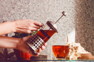 hot tea. the girl pours hot tea from the brewer into the cup. kitchen. home plant