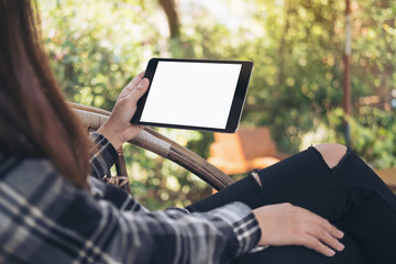 Mockup image of woman's hand holding black tablet pc with blank white screen while sitting outdoor with green nature background