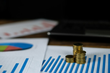 Step of coins stacks with notebook laptop computer and financial graph on white paper on working table, business planning vision and finance analysis concept.