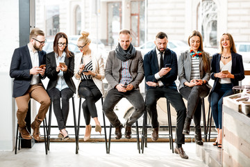 Business people sitting in a row using smartphones near the window in the cafe